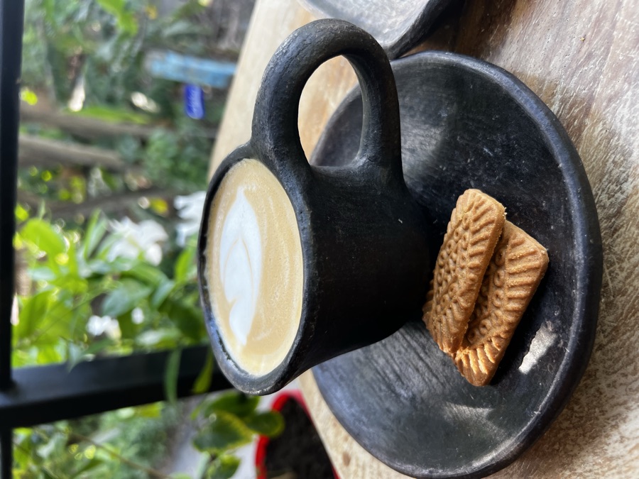Latte in a black clay cup with cookies, tropical greenery behind
