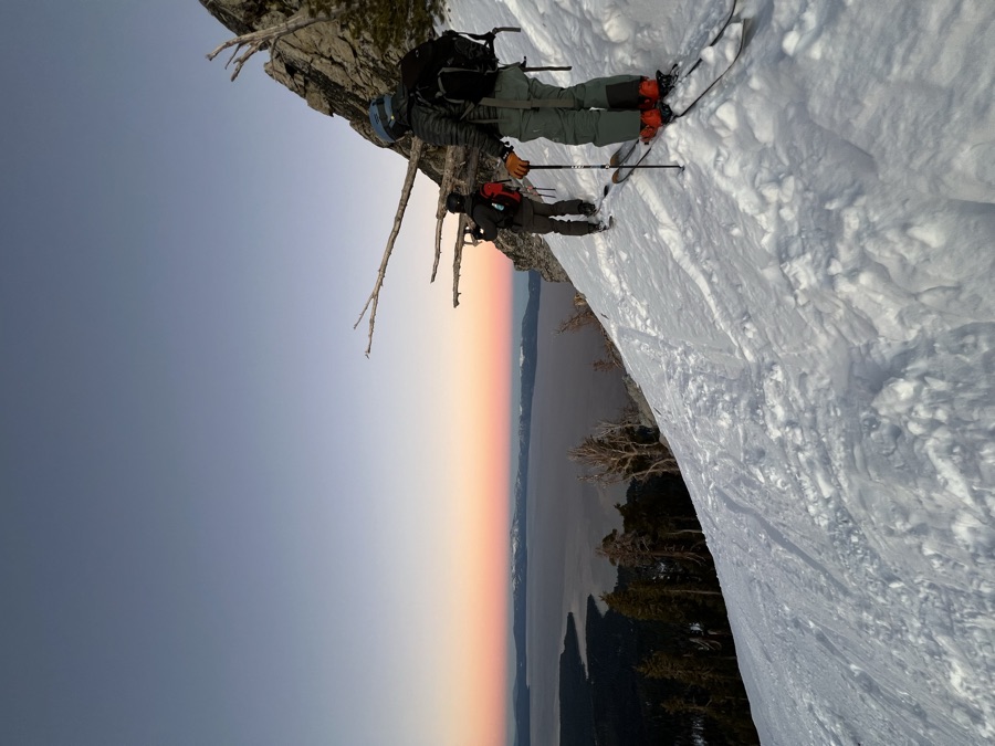 Two backcountry skiers traversing a snowy slope at dusk high above Lake Tahoe