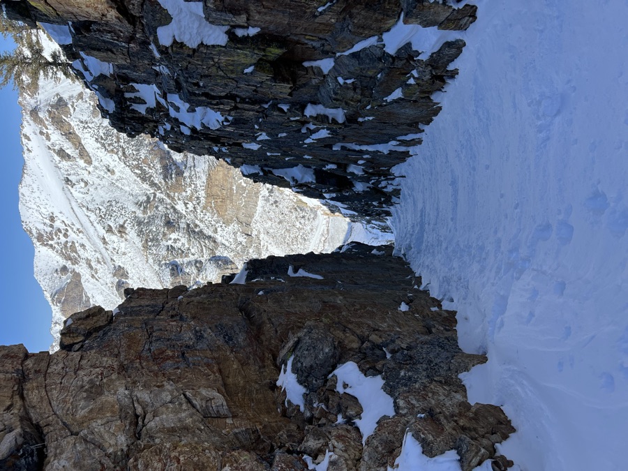 Looking up a steep rocky couloir filled with snow toward a sunlit peak