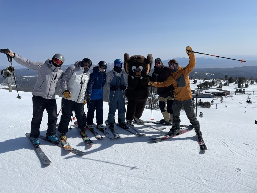 Group of skiers posing with a mountain mascot on a sunny groomed run