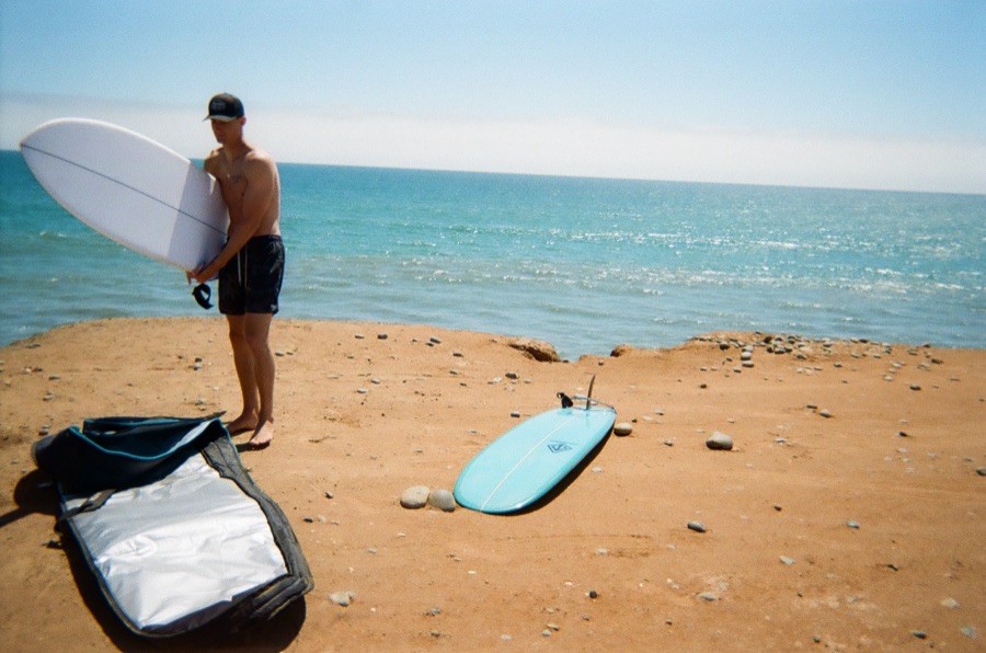 Standing on a red-dirt bluff in Baja with a surfboard, the Pacific behind
