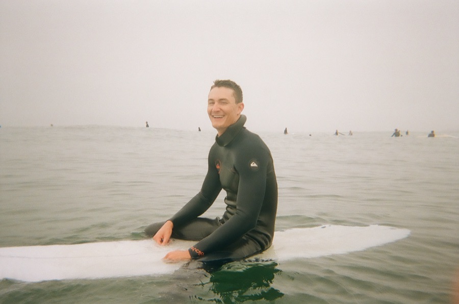 Sitting on a longboard in a foggy lineup, grinning between sets