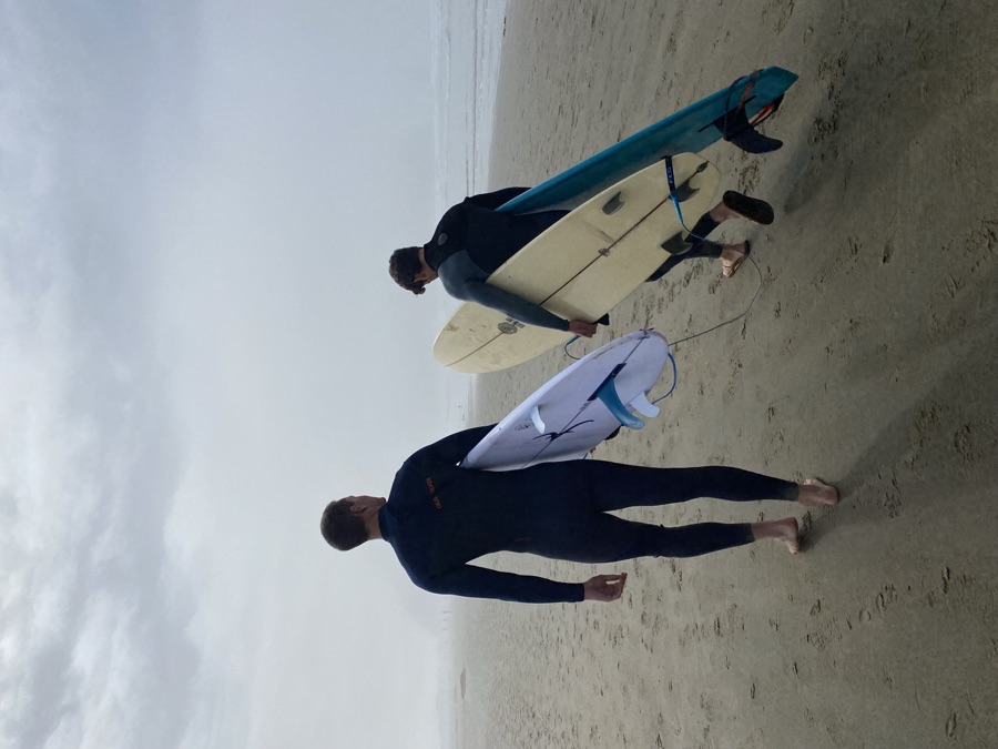 Two surfers walking down a fog-shrouded beach with boards under their arms